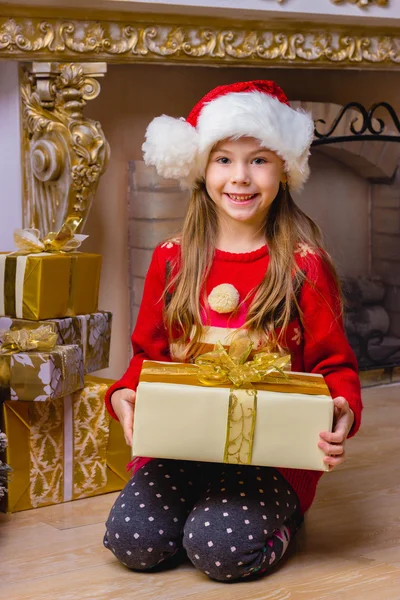 Linda chica feliz en sombrero rojo sosteniendo presente cerca del árbol de Navidad Imágenes De Stock Sin Royalties Gratis