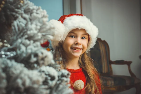 Cute happy girl in red hat near christmas tree — Stock Photo, Image