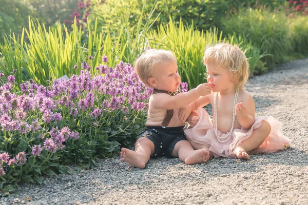 Baby girl and boy sitting in a beautiful garden and sharing snack — Stock Photo, Image