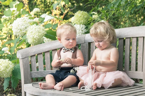 Junge und Mädchen in festlichem Kleid sitzen auf einer Holzbank in einem schönen Garten lizenzfreie Stockfotos