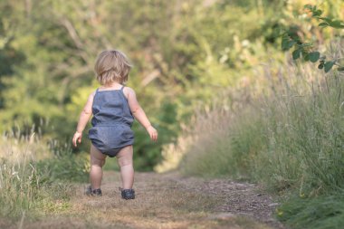 Kız bebek uzak yeşil orman yolu üzerinde yürüyor