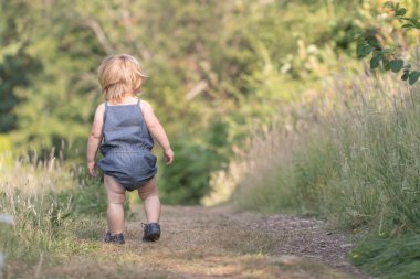 Kız bebek uzak yeşil orman yolu üzerinde yürüyor