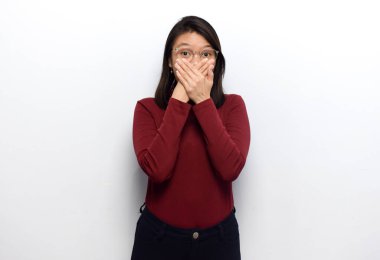 Genç ve güzel Asyalı kadınların elleri ile ağzını kapayarak beyaz arka planda izole edilmiş kırmızı gömlek giyerler.