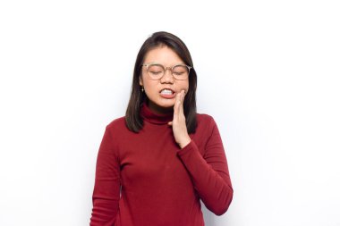 Diş ağrısı ve yanak jesti. Genç Asyalı güzel kadınlar beyaz arka planda izole edilmiş kırmızı gömlek giyerler.