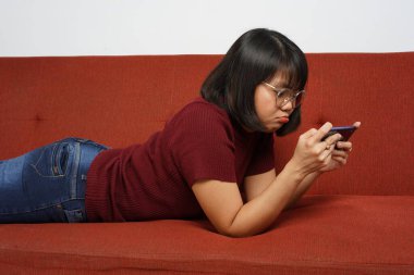 Kırmızı tişört ve mavi kot giyen güzel Asyalı kız akıllı telefondan mobil oyun oynuyor.