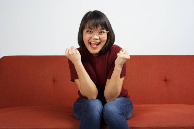 Kırmızı tişörtlü ve mavi kotlu güzel bir Asyalı kız kameraya heyecanlı bir şekilde bakıyor.