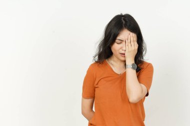 Beyaz arka planda turuncu tişört giyen güzel Asyalı kadın baş ağrısı çekiyor.