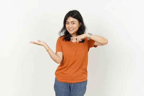 オレンジ色のTシャツを身に着けている美しいアジアの女性白い背景に隔離された手のひらに製品を表示または指す — ストック写真