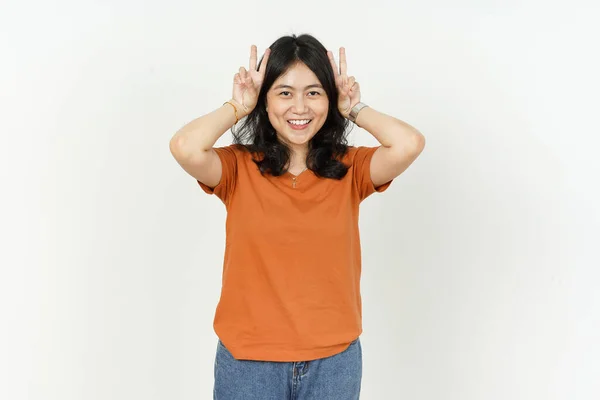 オレンジ色のTシャツを身に着けている美しいアジアの女性は 白い背景に隔離されたウサギの耳として指を使用 — ストック写真