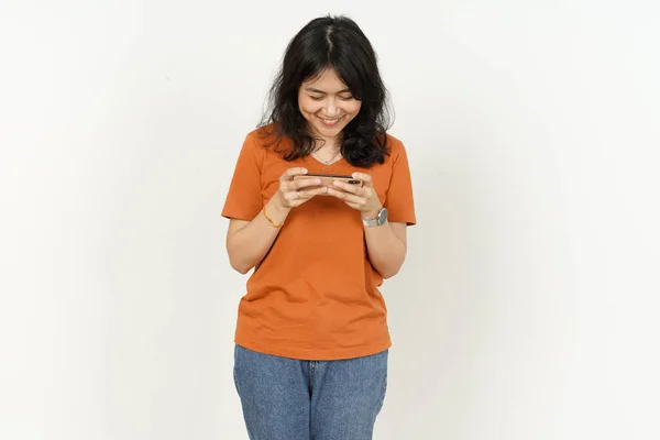 스마트폰으로 게임을 배경에 고립된 오렌지색 티셔츠를 아름다운 아시아 우승을 차지하는 — 스톡 사진