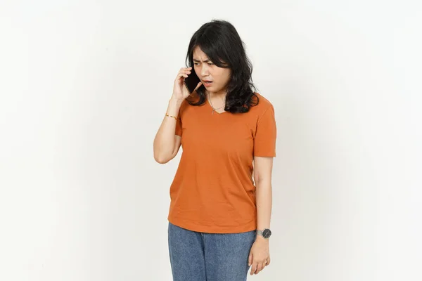 白い背景に孤立したオレンジのTシャツを着た美しいアジア人女性の真剣な怒りの表情で電話で話す — ストック写真