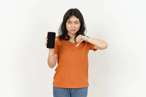 白い背景にオレンジのTシャツを着た美しいアジア人女性の親指ダウンで空白のスマートフォン画面を表示 — ストック写真