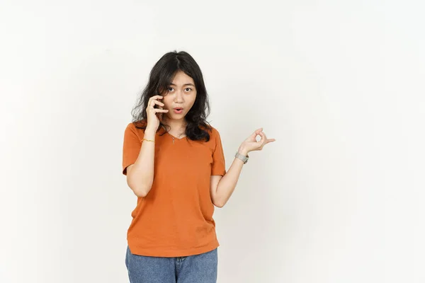 白い背景に孤立したオレンジのTシャツを着た美しいアジア人女性の電話とポインティング側で話す — ストック写真