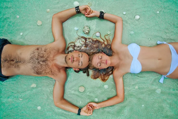 Beautiful couple lying in water with shells on tropic beach — Stock Photo, Image