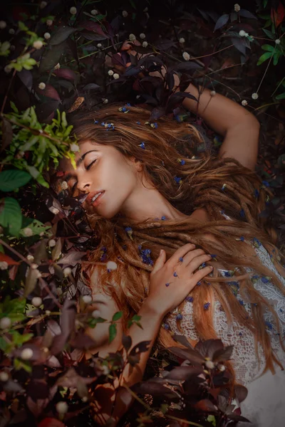 Schönes Mädchen, das auf dem Gras mit Blumen liegt — Stockfoto