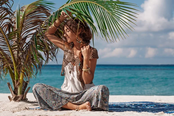 Bella ragazza boho seduto sotto giovane palma sulla spiaggia — Foto Stock