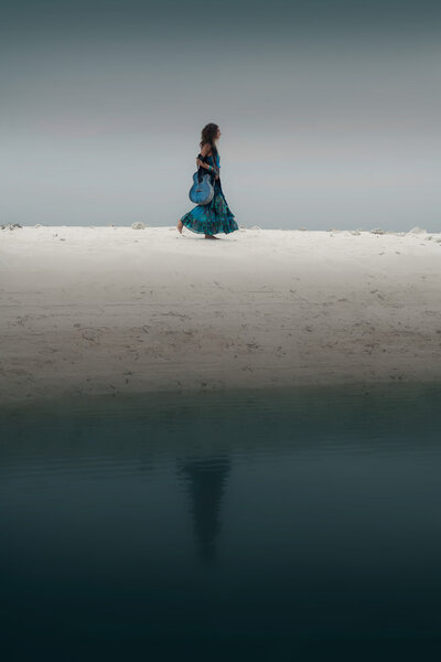 alone woman with guitar walking by the lake shore. 