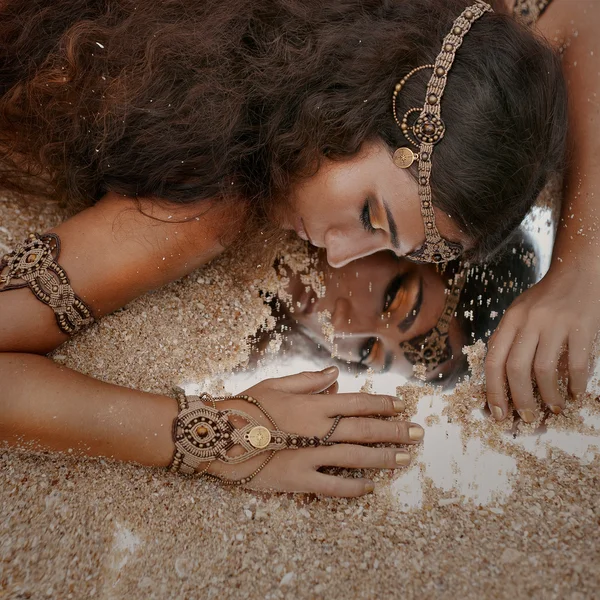 Schönes Mädchen in ethnischem Schmuck und Spiegel mit Sand bedeckt — Stockfoto