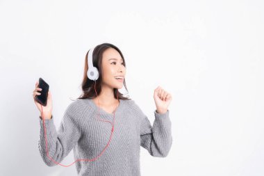 Gri kazak giyen genç güzel bir kadın yalan söylüyor ve beyaz arka planda izole edilmiş beyaz kulaklıklar takarak müzik dinliyor. Rahatlatıcı ve mutlu.