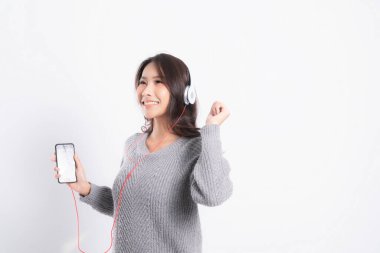 Gri kazak giyen genç güzel bir kadın yalan söylüyor ve beyaz arka planda izole edilmiş beyaz kulaklıklar takarak müzik dinliyor. Rahatlatıcı ve mutlu.