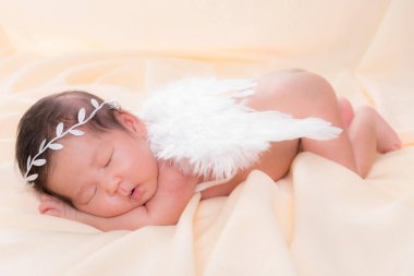 Bir aylık bir bebeğin portresi uyuyor, yeni doğmuş bir kız bebek. Beyaz bir saç bandı takıyor, melek kanatları takıyor ve krem rengi bir battaniyenin üzerinde uyuyor. Yeni doğan stüdyonun konsept portresi.