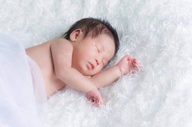 Beyaz bir battaniyenin üzerinde uyuyan, yeni doğmuş bir kızın portresi. Yeni doğan stüdyonun konsept portresi.