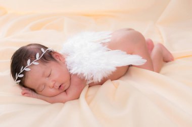 Bir aylık bir bebeğin portresi uyuyor, yeni doğmuş bir kız bebek. Beyaz bir saç bandı takıyor, melek kanatları takıyor ve krem rengi bir battaniyenin üzerinde uyuyor. Yeni doğan stüdyonun konsept portresi.