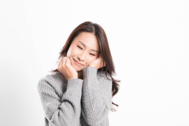 Güzel gülümseyen mutlu Asyalı kadın portresi mükemmel ciltli ve beyaz arka planda izole edilmiş stüdyo çekimlerinde gri bir süveter giyiyor..