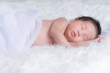 Beyaz bir battaniyenin üzerinde uyuyan, yeni doğmuş bir kızın portresi. Yeni doğan stüdyonun konsept portresi.