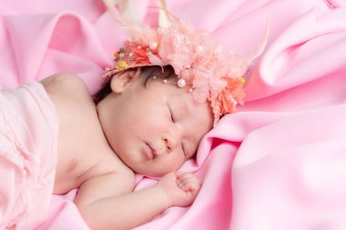 Bir aylık bir bebeğin portresi uyuyor, yeni doğmuş bir kız bebek. Çiçekli bir taç takıyor ve pembe bir battaniyenin üzerinde uyuyor. Yeni doğan stüdyonun konsept portresi.