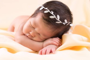 Bir aylık bir bebeğin portresi uyuyor, yeni doğmuş bir kız bebek. Beyaz bir saç bandı takıyor ve krem rengi bir battaniyenin üzerinde uyuyor. Yeni doğan stüdyonun konsept portresi.
