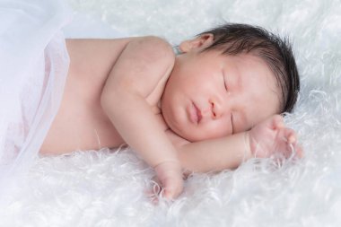 Beyaz bir battaniyenin üzerinde uyuyan, yeni doğmuş bir kızın portresi. Yeni doğan stüdyonun konsept portresi.