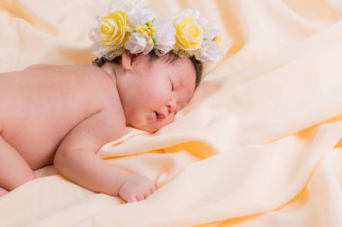Bir aylık bir bebeğin portresi uyuyor, yeni doğmuş bir kız bebek. Çiçekli bir taç takıyor ve krem rengi bir battaniyenin üzerinde uyuyor. Yeni doğan stüdyonun konsept portresi.