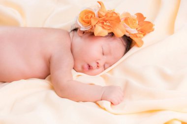 Bir aylık bir bebeğin portresi uyuyor, yeni doğmuş bir kız bebek. Çiçekli bir taç takıyor ve krem rengi bir battaniyenin üzerinde uyuyor. Yeni doğan stüdyonun konsept portresi.