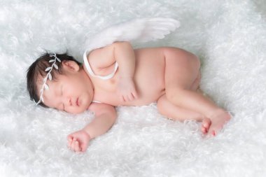 Bir aylık bir bebeğin portresi uyuyor, yeni doğmuş bir kız bebek. Taçlı bir saç bandı takıyor, tüylü melek kanatları takıyor ve beyaz bir battaniyenin üzerinde uyuyor. Yeni doğan stüdyonun konsept portresi.