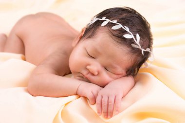 Bir aylık bir bebeğin portresi uyuyor, yeni doğmuş bir kız bebek. Beyaz bir saç bandı takıyor ve krem rengi bir battaniyenin üzerinde uyuyor. Yeni doğan stüdyonun konsept portresi.