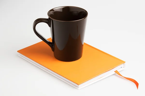 Оранжевая книга записей белой ручкой и чашкой — стоковое фото
