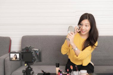 Genç Asyalı güzellik blogcusu, çevrimiçi seyircisine makyaj dersi verirken ayna kullanarak kirpik kıvrımını gösteriyor..