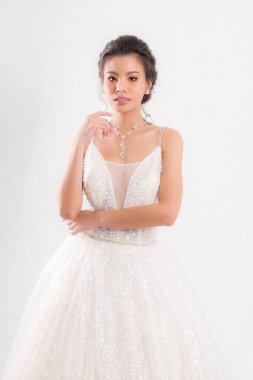 Beyaz gelinlik ve kolyeli güzel Asyalı gelin beyaz arka planda stüdyo çekimlerinde zarif bir poz veriyor..