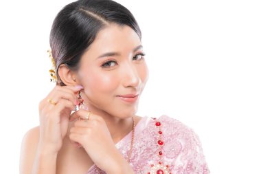 Geleneksel düğün kıyafetli genç Taylandlı güzel kadın zarif küpesini incelikle ayarlıyor ve özel gününe hazırlanıyor..