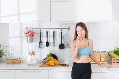 Parlak bir mutfakta meyve suyu içen sağlıklı bir Asyalı kadın evde sabah rutininin tadını çıkarıyor..