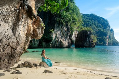 Asyalı bir kadın Lao Lading Adası 'ndaki mavi deniz kıyısındaki kayada oturuyor ve Tayland' ın Krabi Eyaleti 'nde seyahat ediyor.