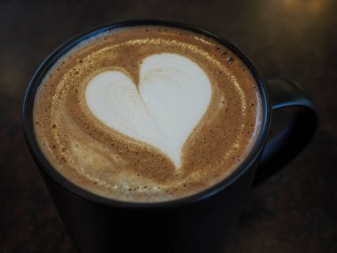 Kahve fincanında kalp şeklinde latte sanatı, masada sıcak latte.