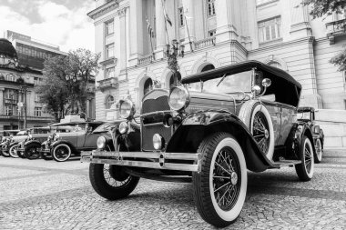 Şehir meydanında zarif bir tarihi binanın önünde dizilmiş klasik klasik klasik klasik arabaların siyah beyaz fotoğrafı. Detaylı krom ve beyaz duvar lastiklerine sahip Retro otomobiller nostaljik bir atmosfer yaratıyor, tarih kavramları ve miras için ideal.