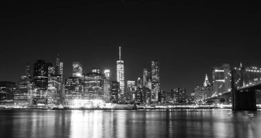 Brooklyn Köprüsü 'nü aydınlatan ve nehri yansıtan New York şehrinin gece manzarası. Modern gökdelenler ve şehir ışıklarıyla uzun süre korunan şehir manzarası. Siyah ve beyaz