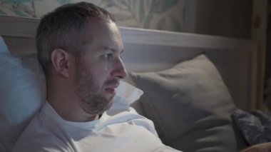 Genç adam uyumadan önce dizüstü bilgisayarla yatakta yatıyor.