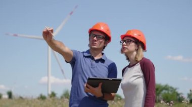 İki ciddi mühendis tartışıyor, tablet kullanıyorlar. Rüzgar türbini elektrik endüstrisinde çalışan kadın ve erkek işçiler. Ekolojik enerji, endüstri gücü, yel değirmeni, tarla işçisi yenilenebilir
