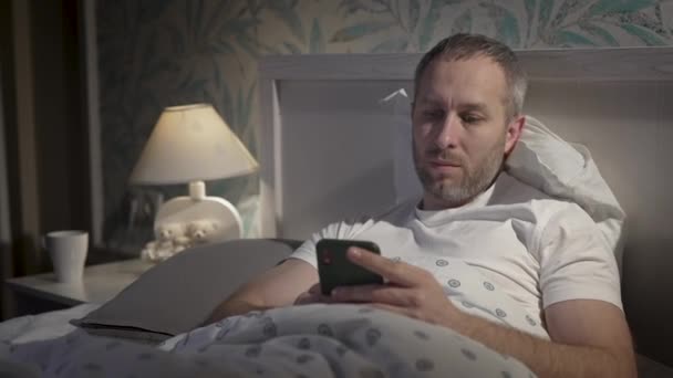 잠 자기전에 스마트폰을 들고 침대에 누워 있는 청년. — 비디오