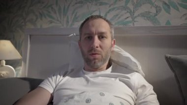 Genç adam uyumadan önce dizüstü bilgisayarla yatakta yatıyor.