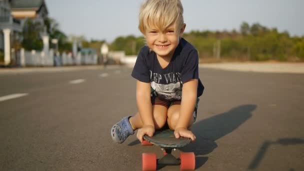 Gelukkig jongetje rijdt zittend op het skateboard in slowmotionx2 — Stockvideo